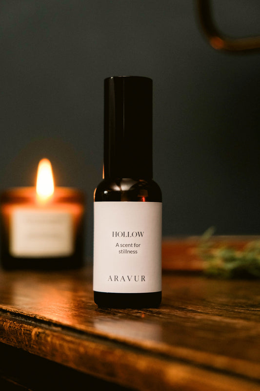Bottle of Aravur 'Hollow' room spray on a wooden surface with a candle in the background